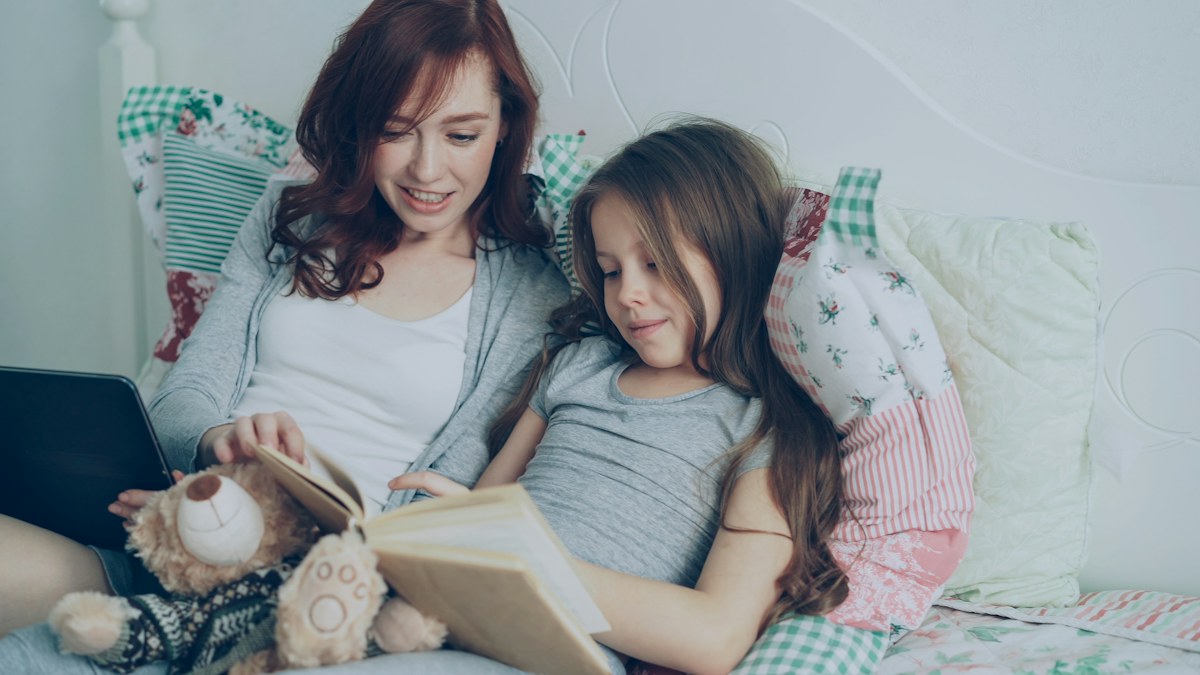 A mother and daughter reading a book together at home.